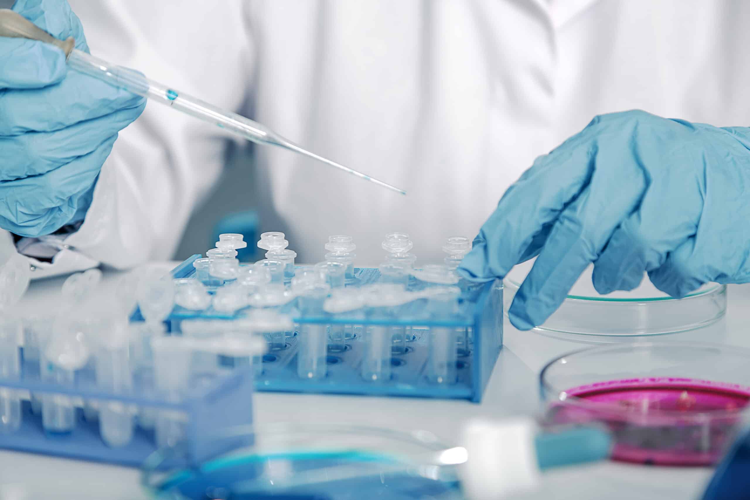May contain a person in blue gloves using a pipette on vials in a blue rack.