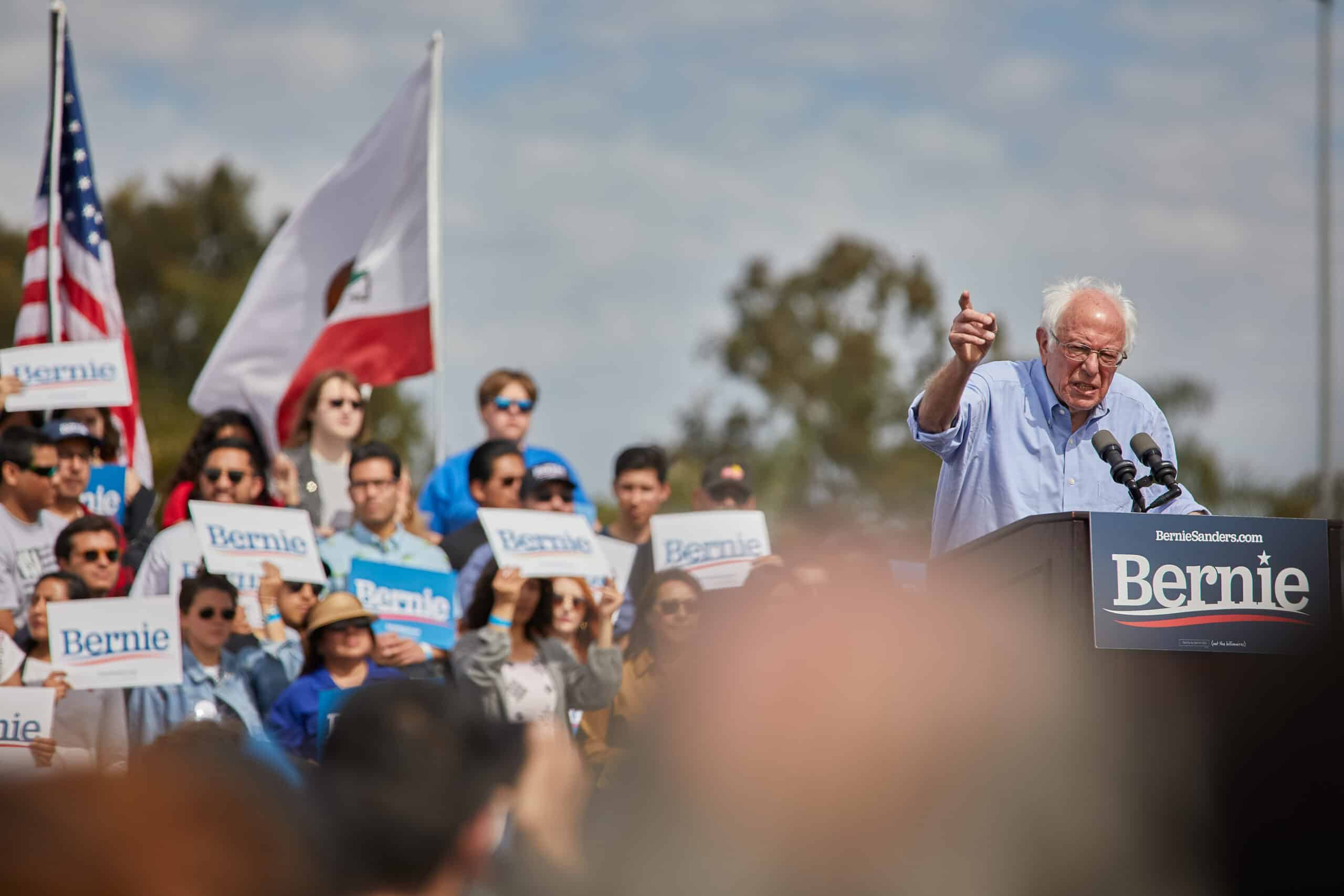 May contain a person speaking at a podium with Bernie signs and American and California flags.