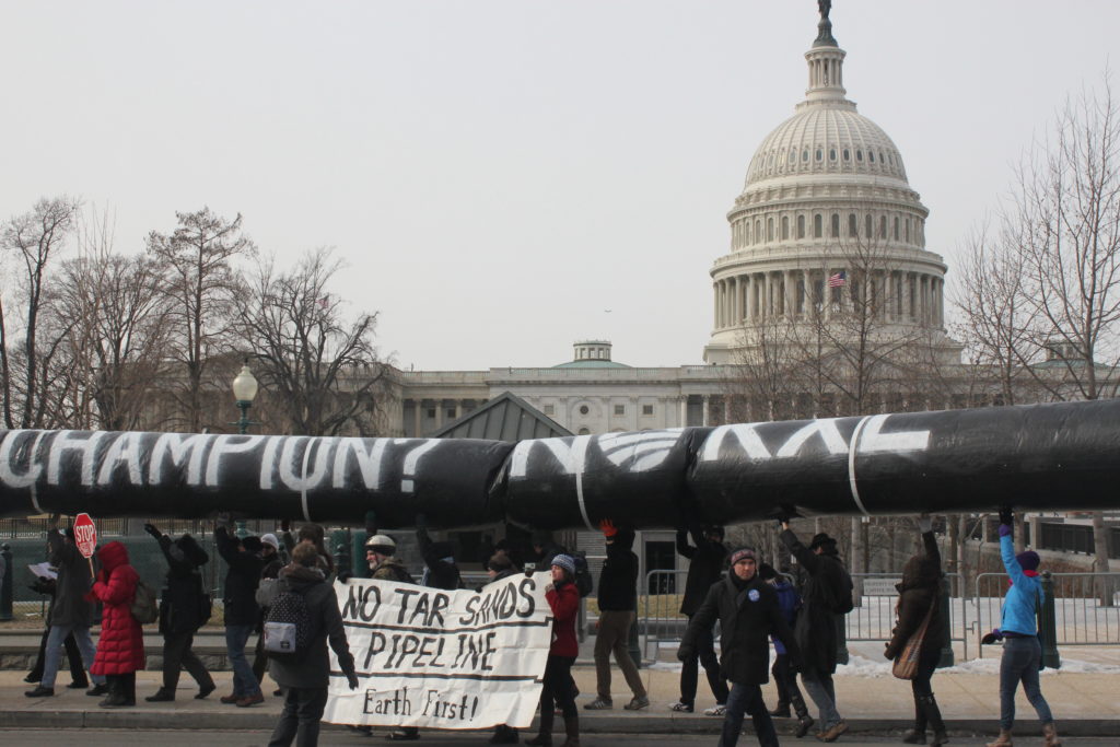 People protesting with a replica pipeline and a sign.