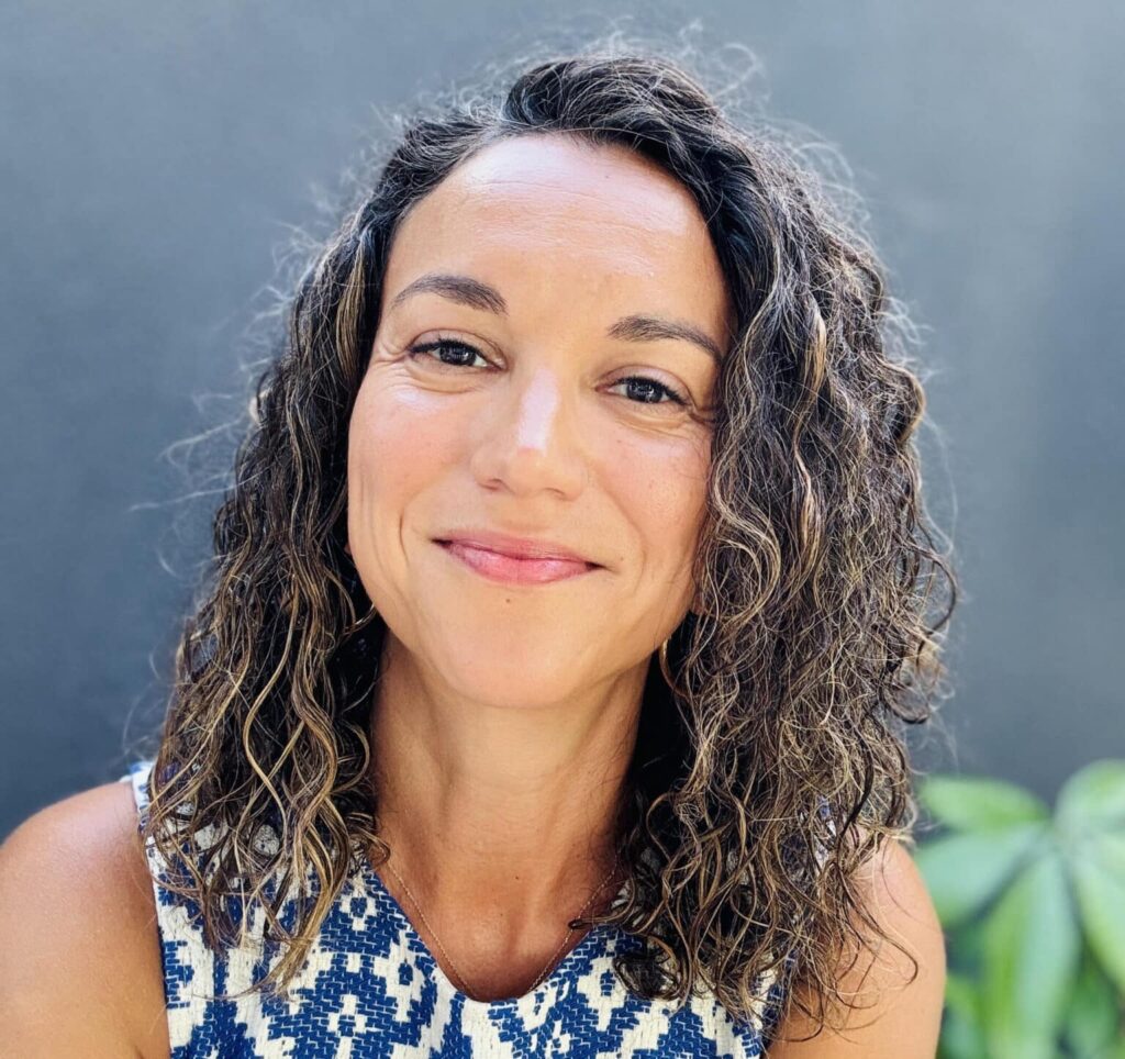 A person with curly hair wearing a blue and white patterned top.