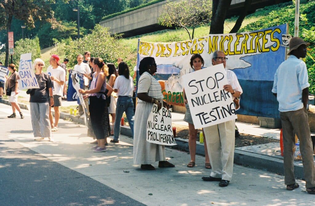 May contain a person holding a sign that says "STOP NUCLEAR TESTING".