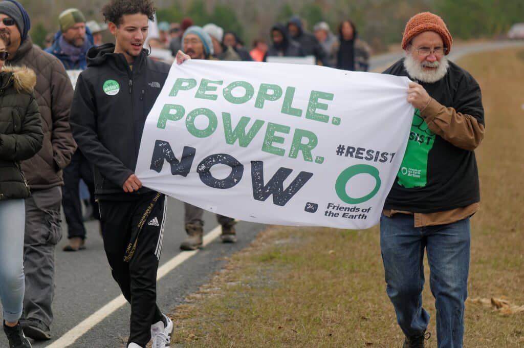 May contain two people holding a banner that says "PEOPLE. POWER. NOW."