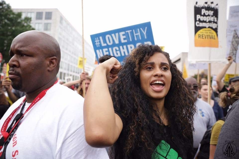 May contain two people at a rally, one is raising their fist.