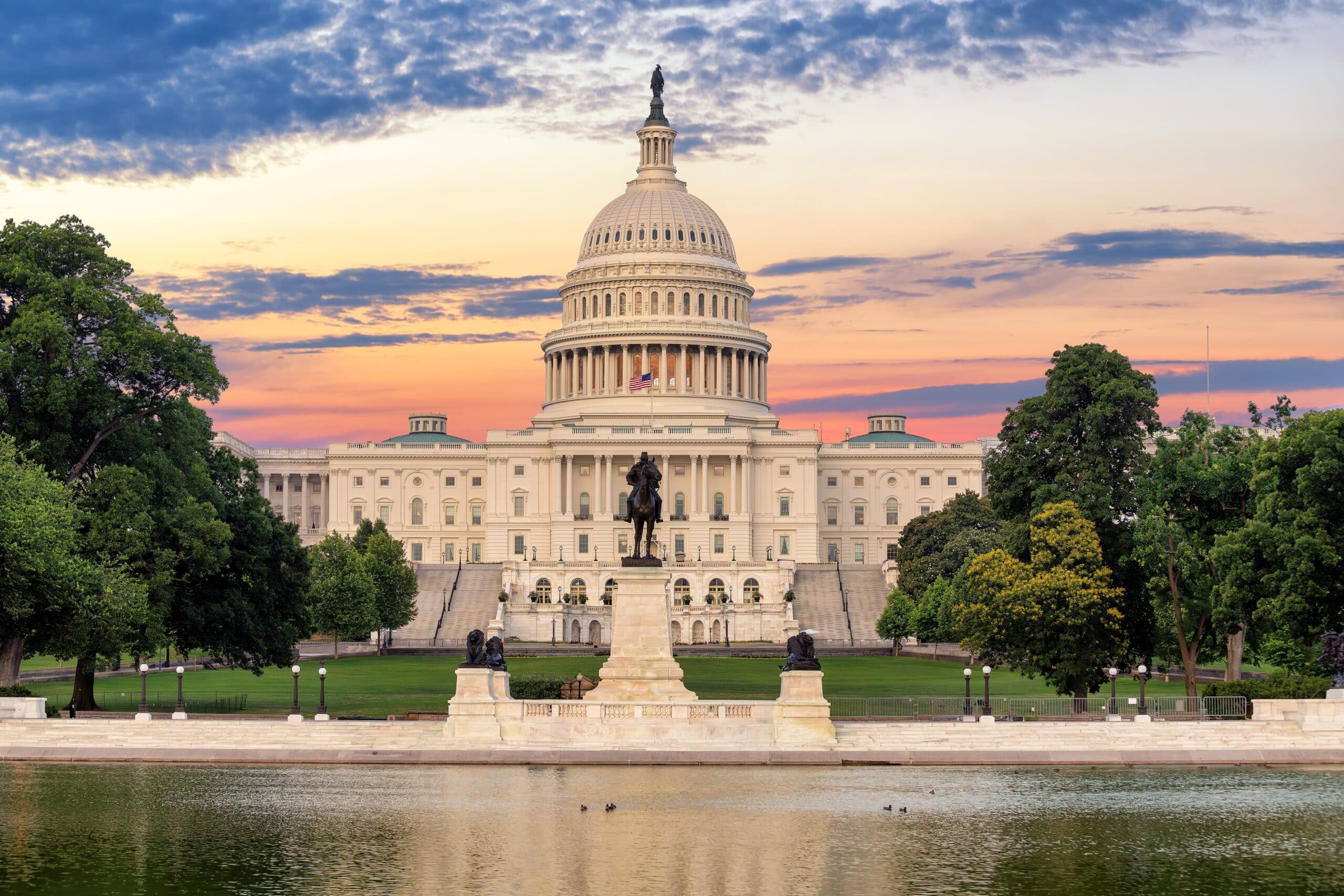 May contain the US Capitol Building with a sunset sky and a pond.