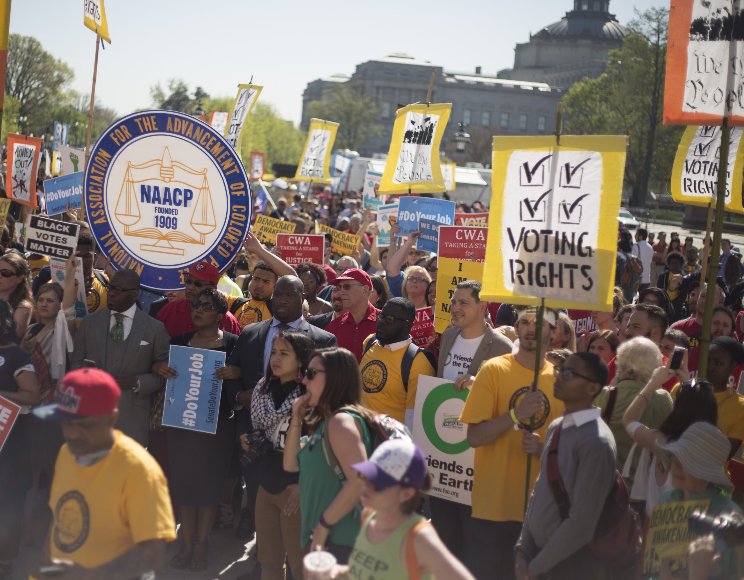 May contain a crowd of people holding signs, including a large NAACP sign and signs about voting rights.