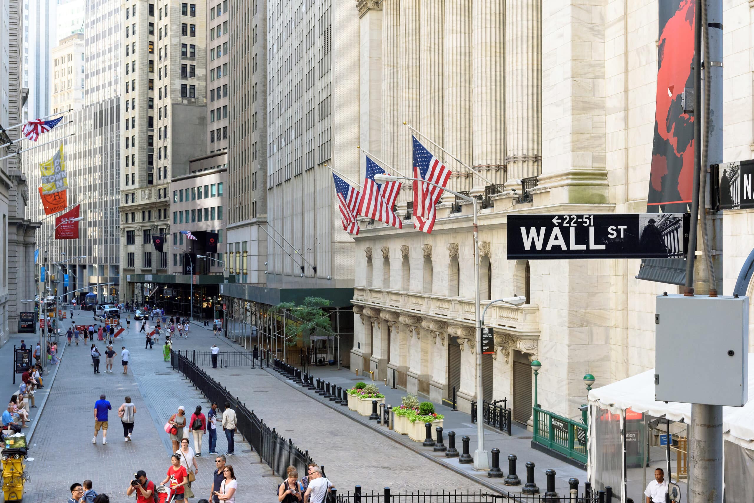 May contain people walking on Wall Street, American flags and a street sign.