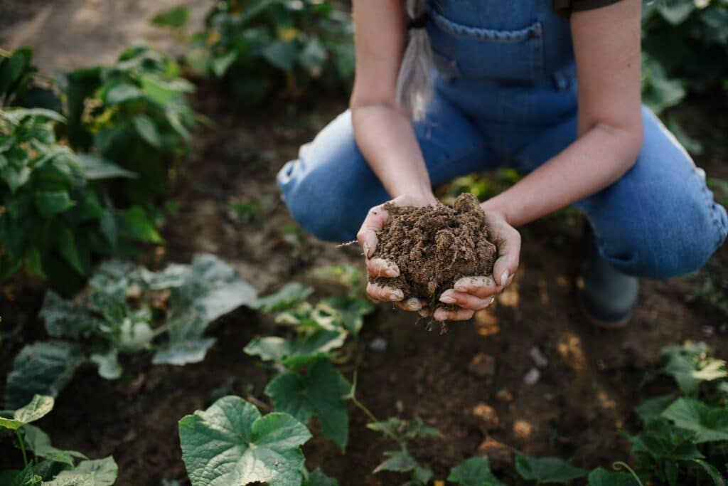 May contain a person in overalls holding soil in a garden.