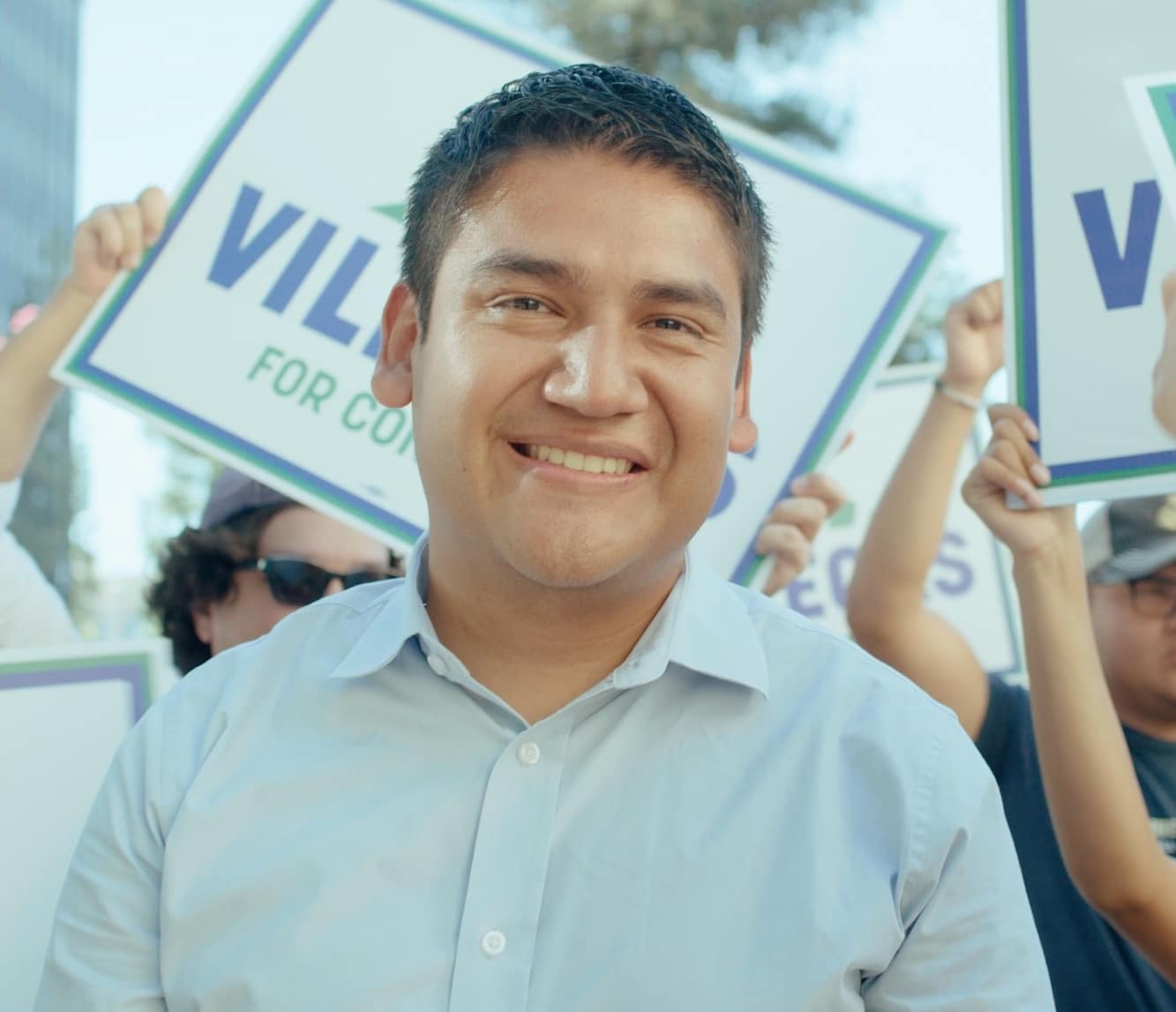 May contain a person smiling, with other people holding campaign signs.