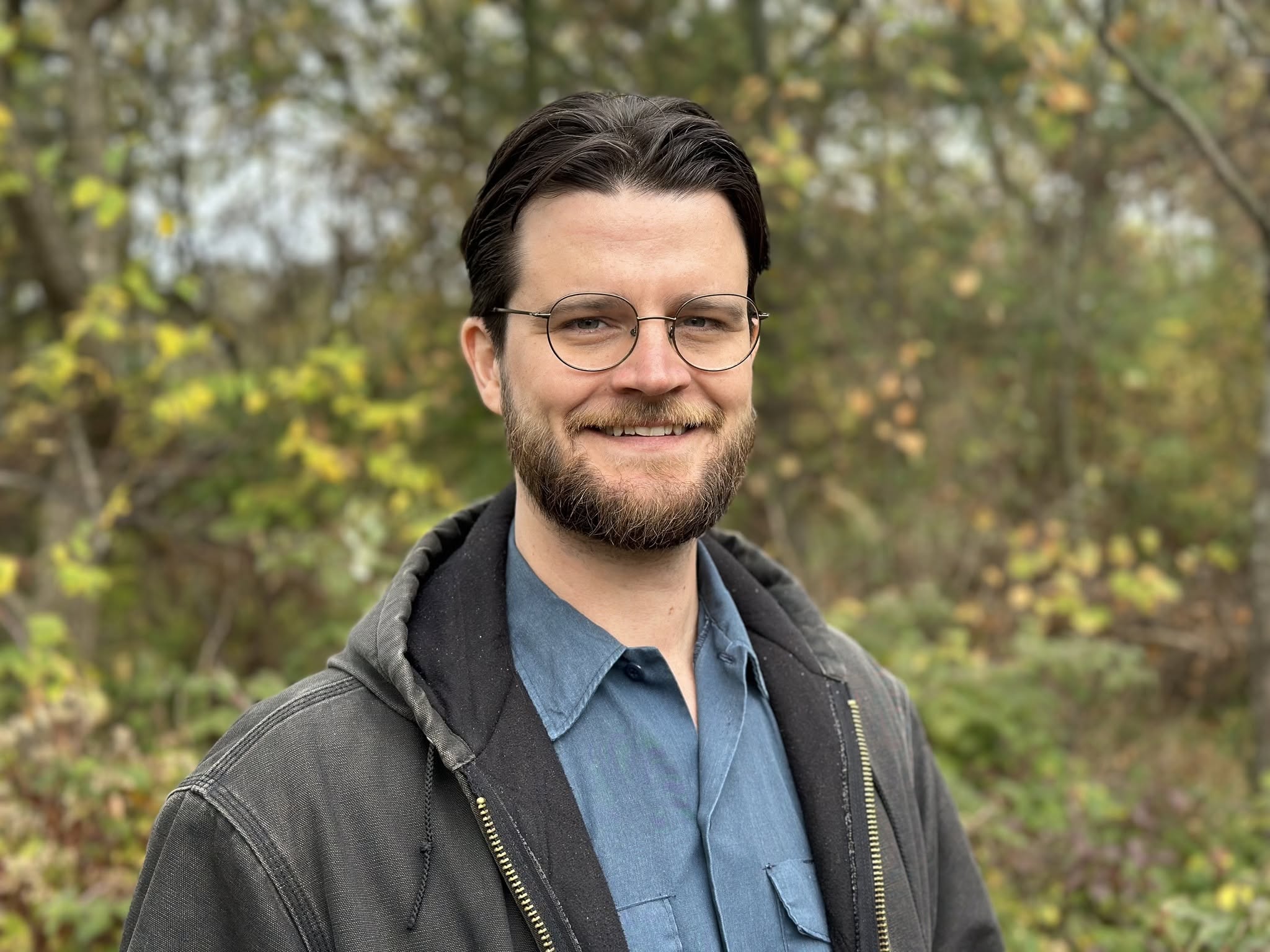 May contain a person with dark hair, beard, and glasses wearing a blue shirt and jacket.